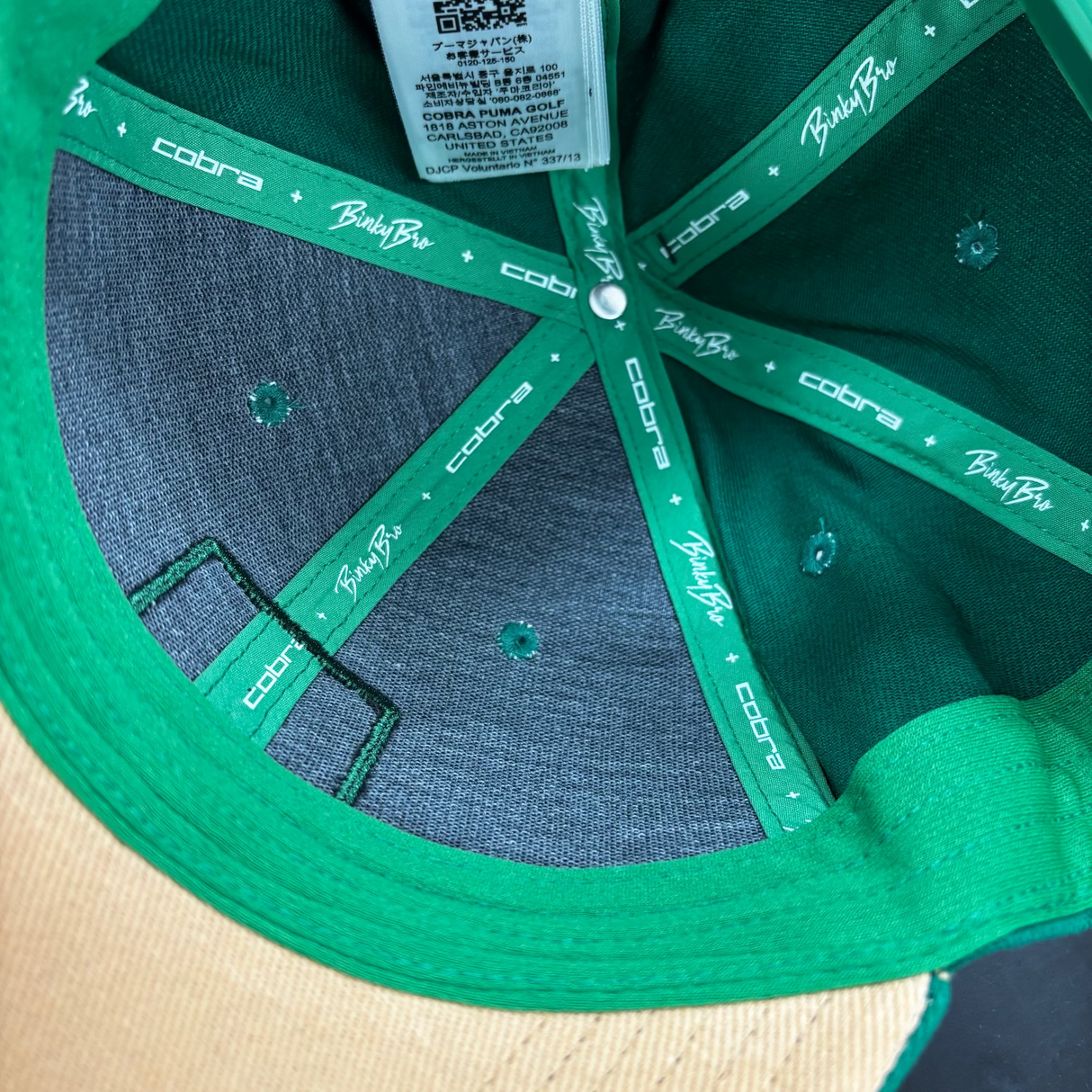 Close-up of a green and beige cap with 'Cobra' branding on the strap.