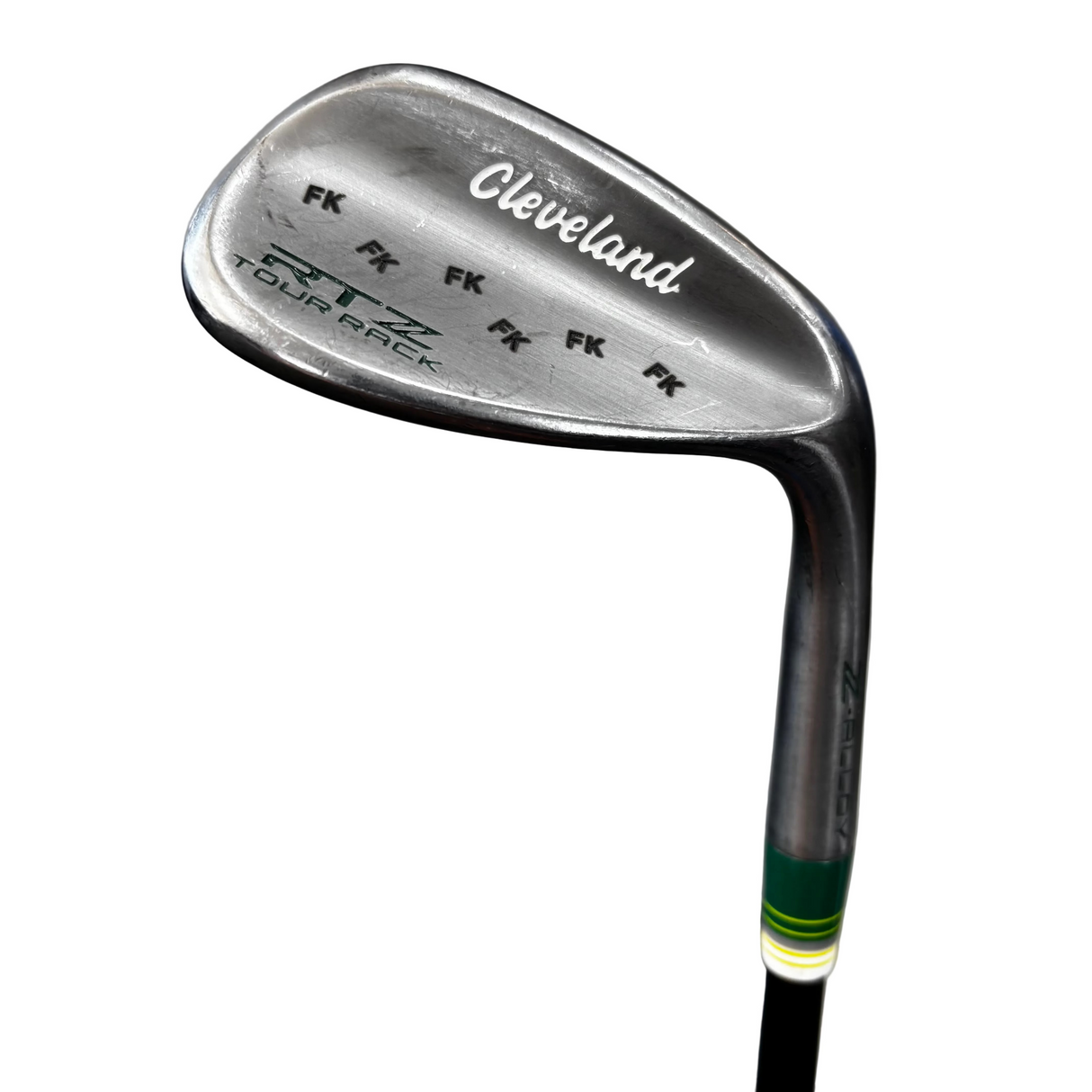 A close-up of a Cleveland Tour rack golf iron club head, showing the metal blade, clubface branding, and part of the shaft with a green and white grip wrap, set against a gray concrete floor with a blue mat in the foreground.