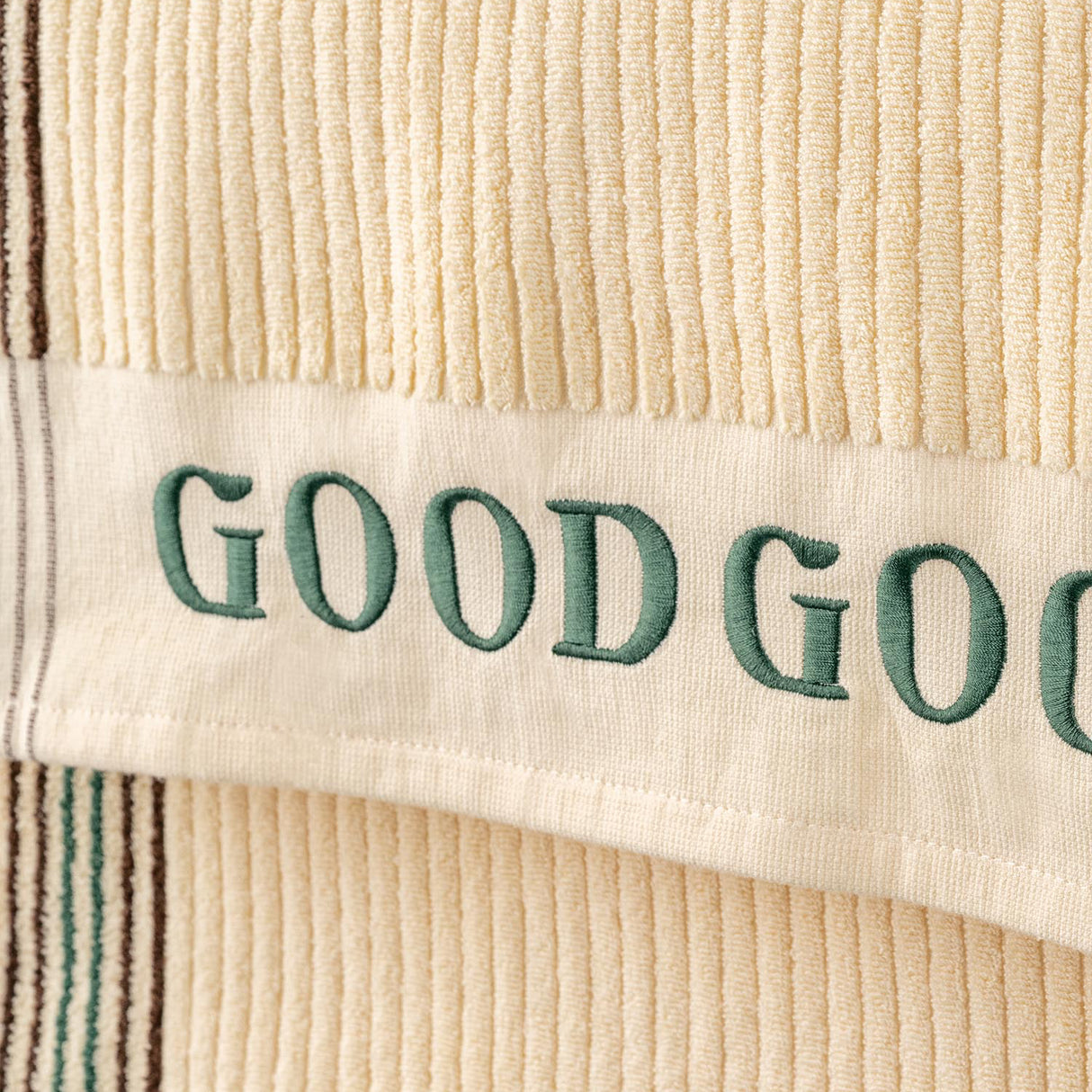 Close-up of a beige fabric with 'GOOD' embroidered in green thread.