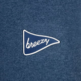 A close-up of a heathered blue fabric surface with a small embroidered pennant-shaped logo in blue and white reading 'breezy'.