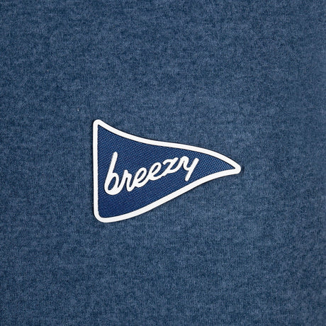 A close-up of a heathered blue fabric surface with a small embroidered pennant-shaped logo in blue and white reading 'breezy'.