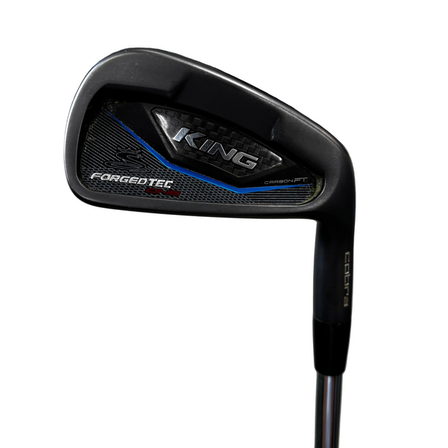 A close-up shot of a Cobra King Forgedtec Iron 7 golf club head, showing the black carbon-fiber textured face with blue and silver accents, set against a blurred indoor background.