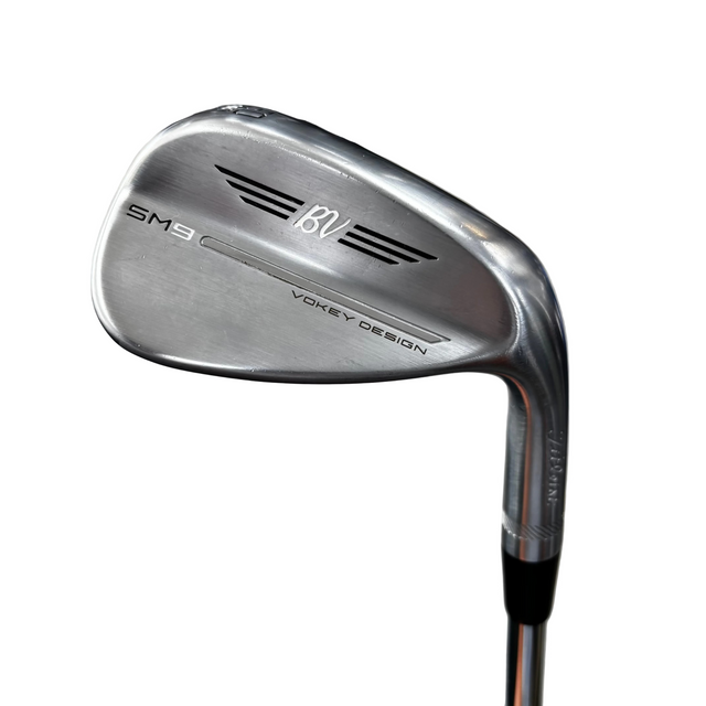 A close-up shot of a silver Callaway SM9 BVI golf wedge with a V-neck design, resting on a golf club stand in a shop setting.