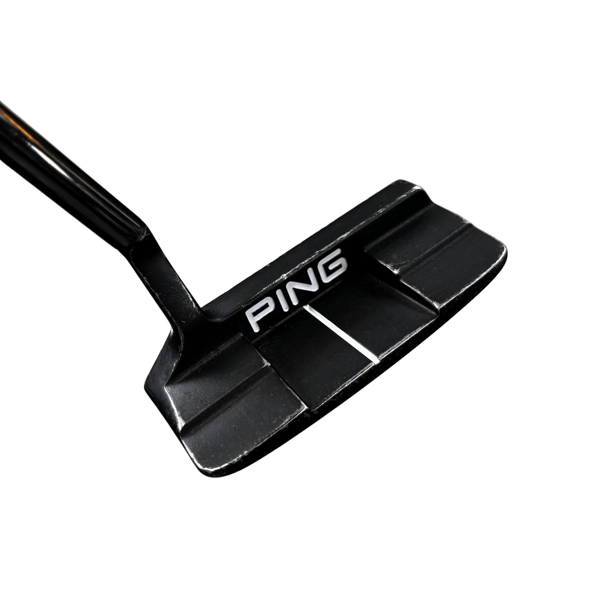 A close-up shot of a black Ping golf putter head with silver lettering, resting on a gray concrete floor with store displays blurred in the background.