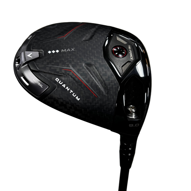 A close-up shot of a Callaway Quantum Max golf driver head, featuring a black carbon fiber pattern with red and white accents, resting on a gray concrete floor.