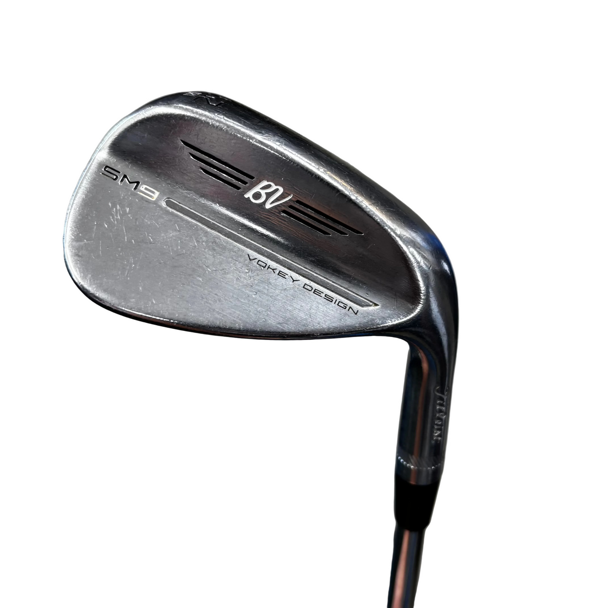 A close-up shot of a titleist SM9 BV golf iron wedge, showing the club head and part of the shaft against a gray concrete floor background.