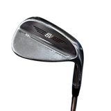A close-up shot of a titleist SM9 BV golf iron wedge, showing the club head and part of the shaft against a gray concrete floor background.