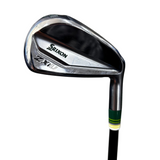 A close-up shot of a Srixon ZXi golf iron club head, showing the polished metal finish, brand name, and model number, with part of the black and green wrapped shaft visible against a gray concrete background.