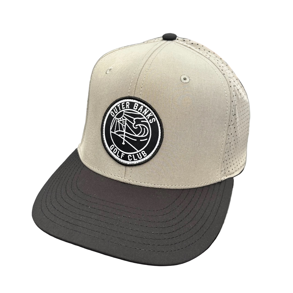 Beige and black cap with a logo on a black surface, with clothing and a laptop in the background.