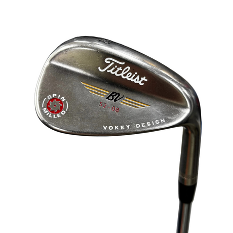 A close-up of a Titleist BV SPIN HITSGED golf wedge, showing the metallic silver metal head with engraved branding and the Vokey Design logo, set against a blurred indoor background.