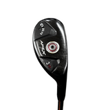 A close-up of a black Apex 3-wood golf club head with white and red branding details, standing on a stand in a golf shop with a concrete floor and bags in the background.