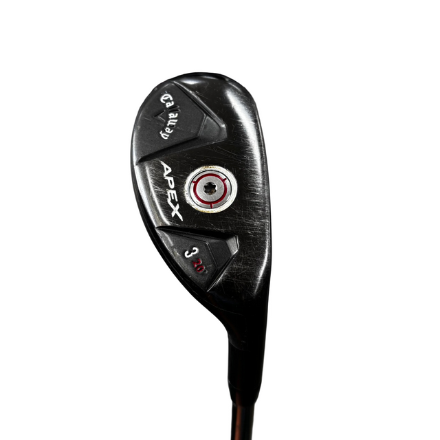 A close-up of a black Apex 3-wood golf club head with white and red branding details, standing on a stand in a golf shop with a concrete floor and bags in the background.