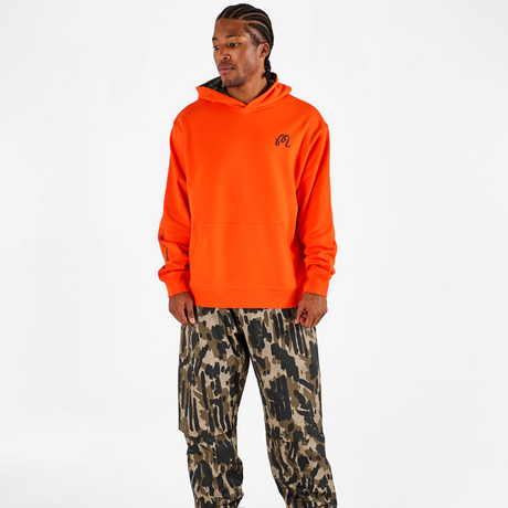 Person wearing an orange hoodie and camouflage pants on a white background