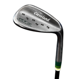 A close-up of a Cleveland  Tour rack golf iron club head, showing the metal blade, clubface branding, and part of the shaft with a green and white grip wrap, set against a gray concrete floor with a blue mat in the foreground.