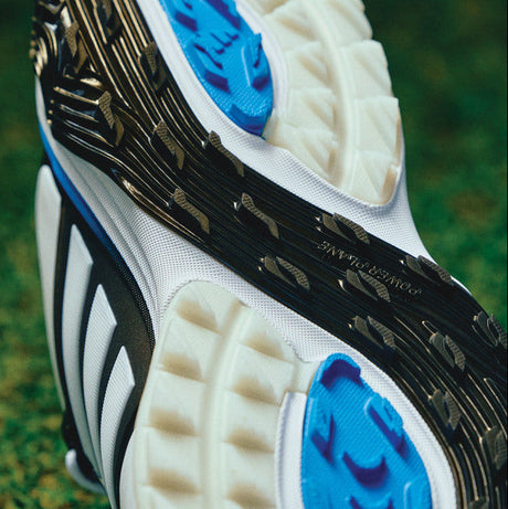Close-up of a black and white Adidas soccer cleat with blue accents on grass.