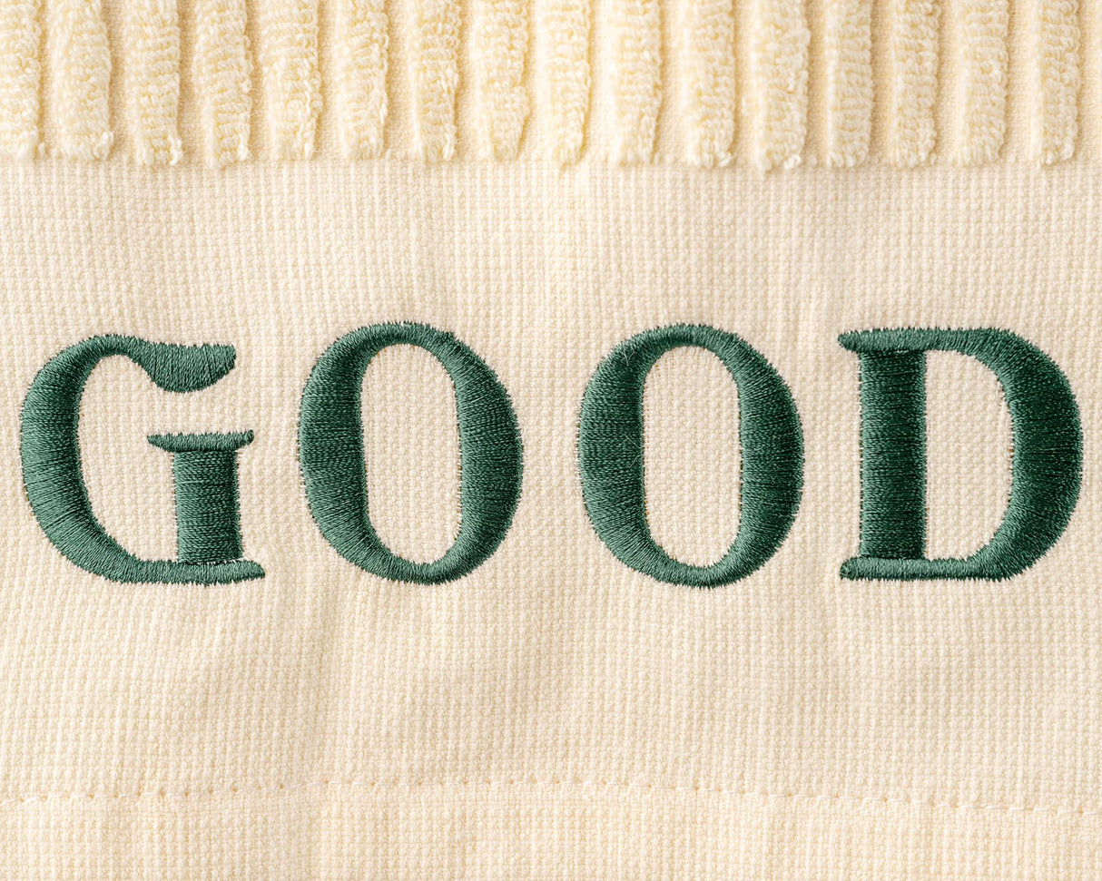 Text 'GOOD' embroidered in green on a beige fabric background