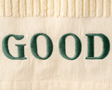Text 'GOOD' embroidered in green on a beige fabric background