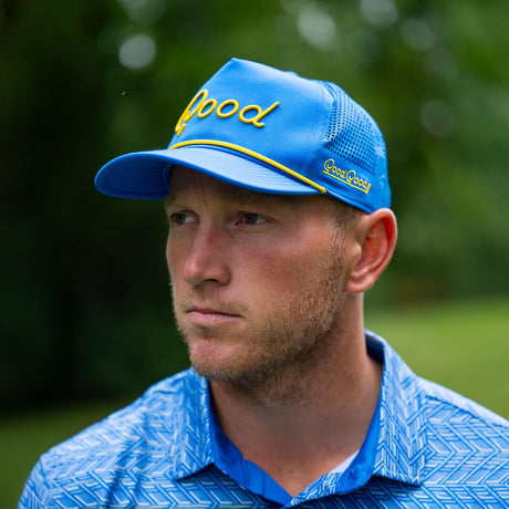 Man wearing a blue cap with 'Good' branding in an outdoor setting